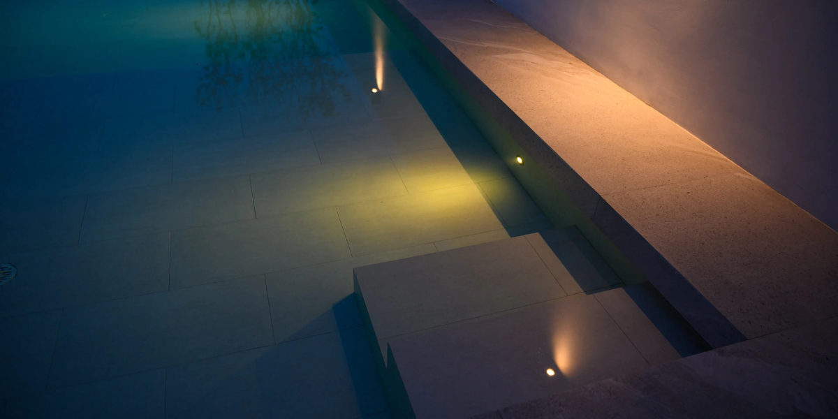 Piscine éclairée la nuit avec projecteurs Poolplanet : projecteurs à visser, en saillie, ampoules PAR56, éclairages pour piscines hors-sol, coffrets de contrôle et enjoliveurs pour une ambiance lumineuse.